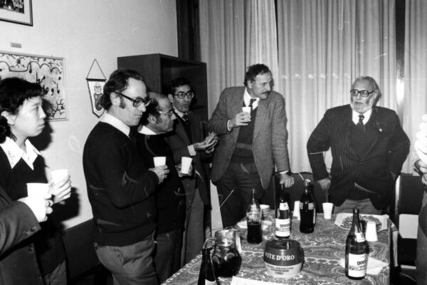 Experimental verification of Salam's electroweak theory, 1983 Scientists L. Bertocchi, G.C. Ghirardi, H.R. Dalafi, L. Fonda and Abdus Salam celebrating together. They stand in a meeting room, surrounding a table with wine and soda. They are engaged in conversation.