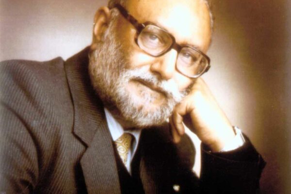 Abdus Salam, 1986 A portrait of Abdus Salam taken in 1986. It is sepia-toned but coloured. Salam rests his hand on his hand as he looks into the camera, against a neutral brown background.