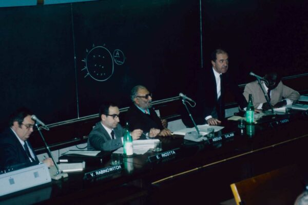 ICTP workshop, 1985 Paolo Tarony speaking at a workshop. He is standing at a speaker's podium, speaking into a microphone. He stands in front of a chalkboard, and next to Salam.