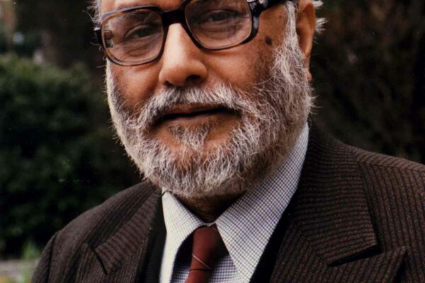 Abdus Salam at the ICTP A portrait of Salam as he stands outside the ICTP. The viewer can see some blurred foliage in the background. Salam is dressed in a wool jacket with an assortment of pens in his breast pocket.