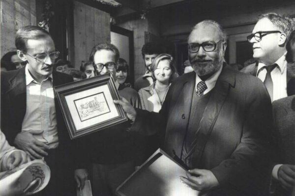 Salam at the ICTP, after winning the Nobel Prize, 1979 Abdus Salam holds up a framed drawing of a castle, showing it to the other staff at the ICTP. He is surrounded by a large group of people who look on.