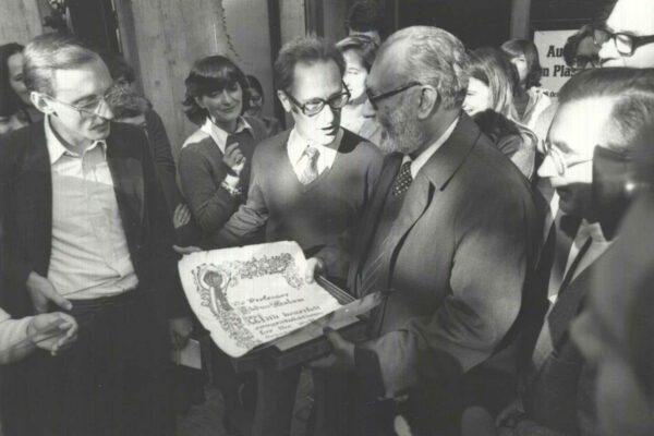 Salam at the ICTP, after winning the Nobel Prize, 1979 Abdus Salam holds up the Nobel Prize certificate, showing it to the other staff at the ICTP. He is surrounded by a large group of people who look on.